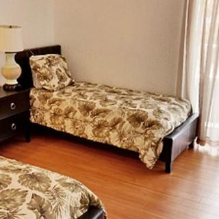 A cozy bedroom featuring twin beds with patterned bedding, a nightstand with a lamp, and wooden floors.