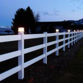 A white fence illuminated by lights during the evening.
