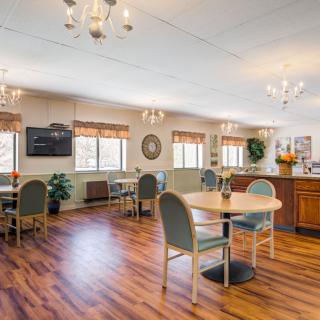 A spacious dining area with multiple tables and chairs, decorated with chandeliers and hardwood flooring.