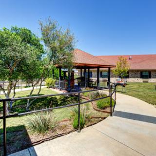 A sunny day showcasing a well-maintained outdoor area with a pathway leading to a building surrounded by greenery.