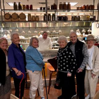 A group of elderly individuals standing in front of a restaurant kitchen with a smiling chef in the background.