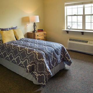 A cozy bedroom with a neatly made bed, bedside table, and a window letting in natural light.