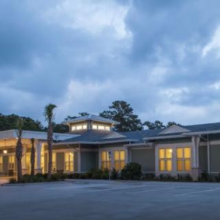 A lit building with trees in the background under a cloudy evening sky.