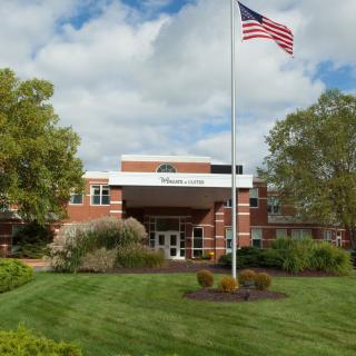 A building with an American flag surrounded by a well-maintained landscape of grass and trees under a cloudy sky.
