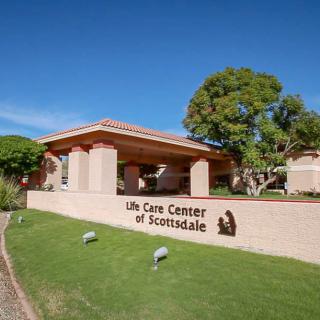 Exterior view of the Life Care Center of Scottsdale, surrounded by a green lawn and trees under a clear blue sky.