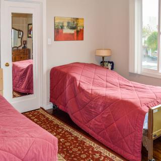 A cozy bedroom with twin beds covered in red bedding, featuring a mirror, lamp, and a window with natural light.