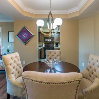 A cozy dining room with a round table, tufted chairs, and overhead chandelier lighting.