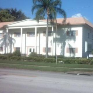 A sunny view of a building with columns and palm trees.