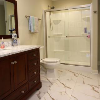 A modern bathroom with a marble floor, featuring a glass-enclosed shower, a toilet, and a wooden vanity with a mirror.