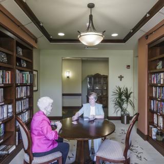 Two people sitting at a table in a library, engaged in conversation.