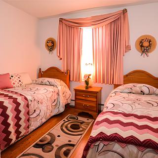 A cozy bedroom featuring twin beds with patterned bedspreads, a nightstand, and decorative curtains.