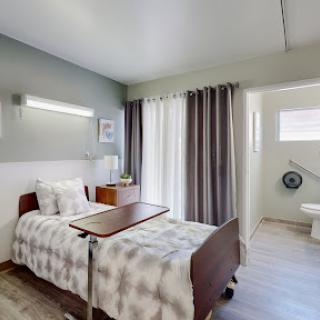 A well-lit hospital room featuring a single bed with a bedside table, curtains for privacy, and an en-suite bathroom.