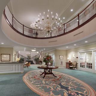 A luxurious hotel lobby featuring a grand chandelier, elegant decor, and a curved staircase.