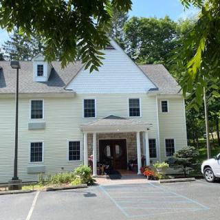 A two-story residential building surrounded by trees with a car parked in front.