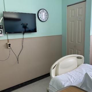 A patient room featuring a hospital bed, a television, and a wall clock.