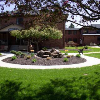 A well-maintained garden with a circular rock feature surrounded by grass and a pathway.
