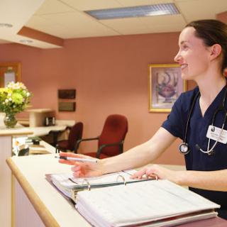 A nurse at the reception desk of a healthcare facility, assisting visitors.