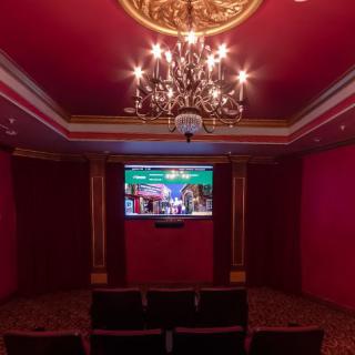 A luxurious home theater with red walls and a chandelier, featuring comfortable seating and a large screen.
