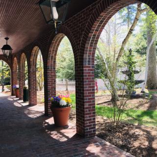 A brick archway pathway with potted plants leads to a sunlit garden.