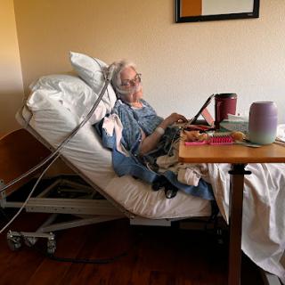 An elderly patient in a hospital room, seated in a hospital bed with medical equipment.