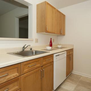 A clean and minimalist kitchen with wooden cabinets, a white countertop, a sink, and a dishwasher.