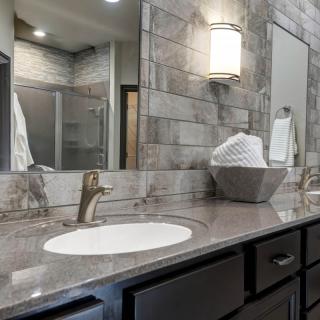 A modern bathroom with a sleek vanity and mirror, featuring elegant lighting and a stone countertop.
