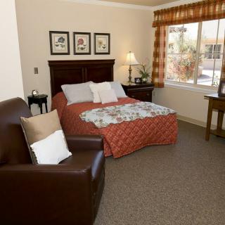 A cozy bedroom with a bed, armchair, and window, featuring warm decor and soft lighting.