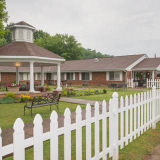 A view of a building with a white picket fence and garden benches in the foreground.