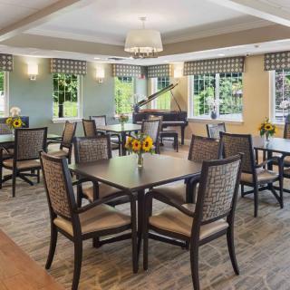 A spacious dining room with wooden tables and chairs, featuring large windows and a piano.