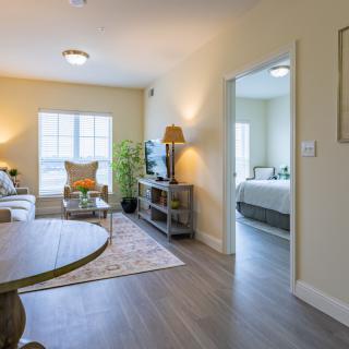 A cozy and well-lit living room with a view into an adjacent bedroom, featuring modern furniture and decor.