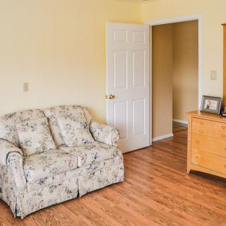 A cozy living room with a floral-patterned sofa, a wooden dresser, and an open door leading to another room.