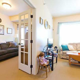 A cozy living room with a sofa, coffee table, and decorative items, featuring French doors and a doll on a chair.