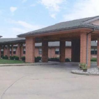 A wide driveway leads to the entrance of a brick building under a partly cloudy sky.