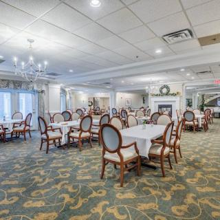 A spacious and elegant restaurant dining room with neatly arranged tables and chairs, featuring a chandelier and carpeted flooring.