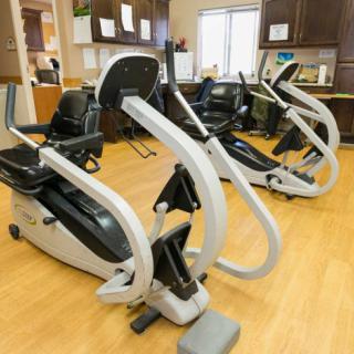 A fitness center with elliptical machines lined up on a wooden floor.
