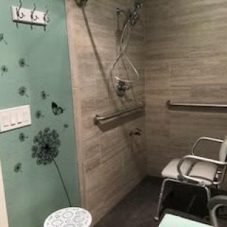 An accessible bathroom with a shower seat and grab bars, featuring decorative elements on a green wall.