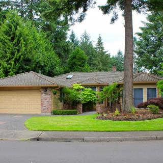 A suburban one-story house with a well-maintained front lawn and tall trees.