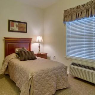 A cozy bedroom with a single bed, a lamp on a bedside table, and a window with curtains.