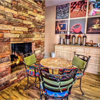 A cozy room featuring a stone fireplace, a round table with colorful chairs, and a coffee station with artwork on the walls.