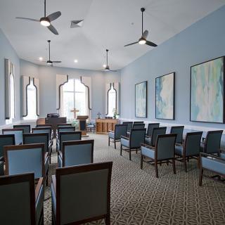 A neatly arranged meeting room with chairs facing a podium, ceiling fans, and artwork on the walls.