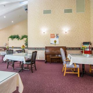 A cozy dining area with tables, chairs, and a piano against a carpeted floor.