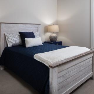 A cozy bedroom with a neatly made bed, featuring navy and white bedding, accompanied by a bedside lamp on a nightstand.