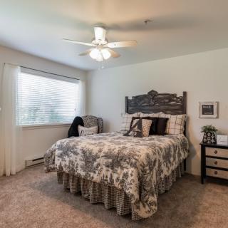 A cozy bedroom with a neatly made bed, a ceiling fan, and natural light streaming in through the window.