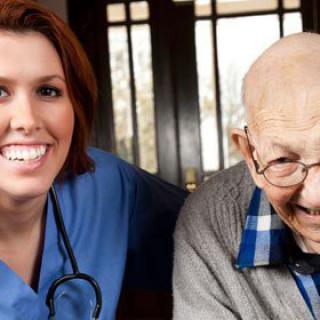 A nurse provides care and support to an elderly man, both smiling warmly.