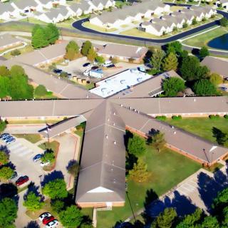 Aerial view of a complex building structure surrounded by trees and parking areas within a residential neighborhood.