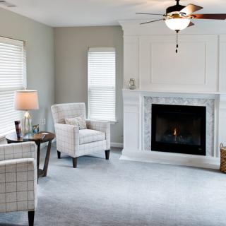 A modern living room featuring a cozy fireplace, armchairs, and natural light from two windows.