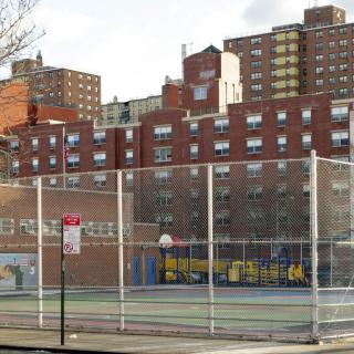 A fenced basketball court in an urban setting with surrounding apartment buildings.