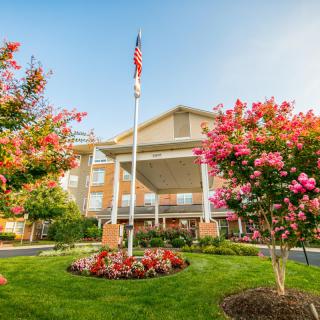 A building with a well-maintained garden featuring colorful flowers and trees, accompanied by a flagpole displaying the American flag.