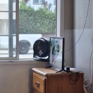 A cozy indoor setup featuring a fan and a computer monitor by the window, offering a glimpse of the outside urban environment.