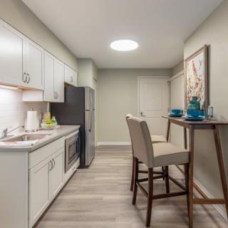 A modern kitchen with sleek white cabinets and a compact dining area featuring bar stools.
